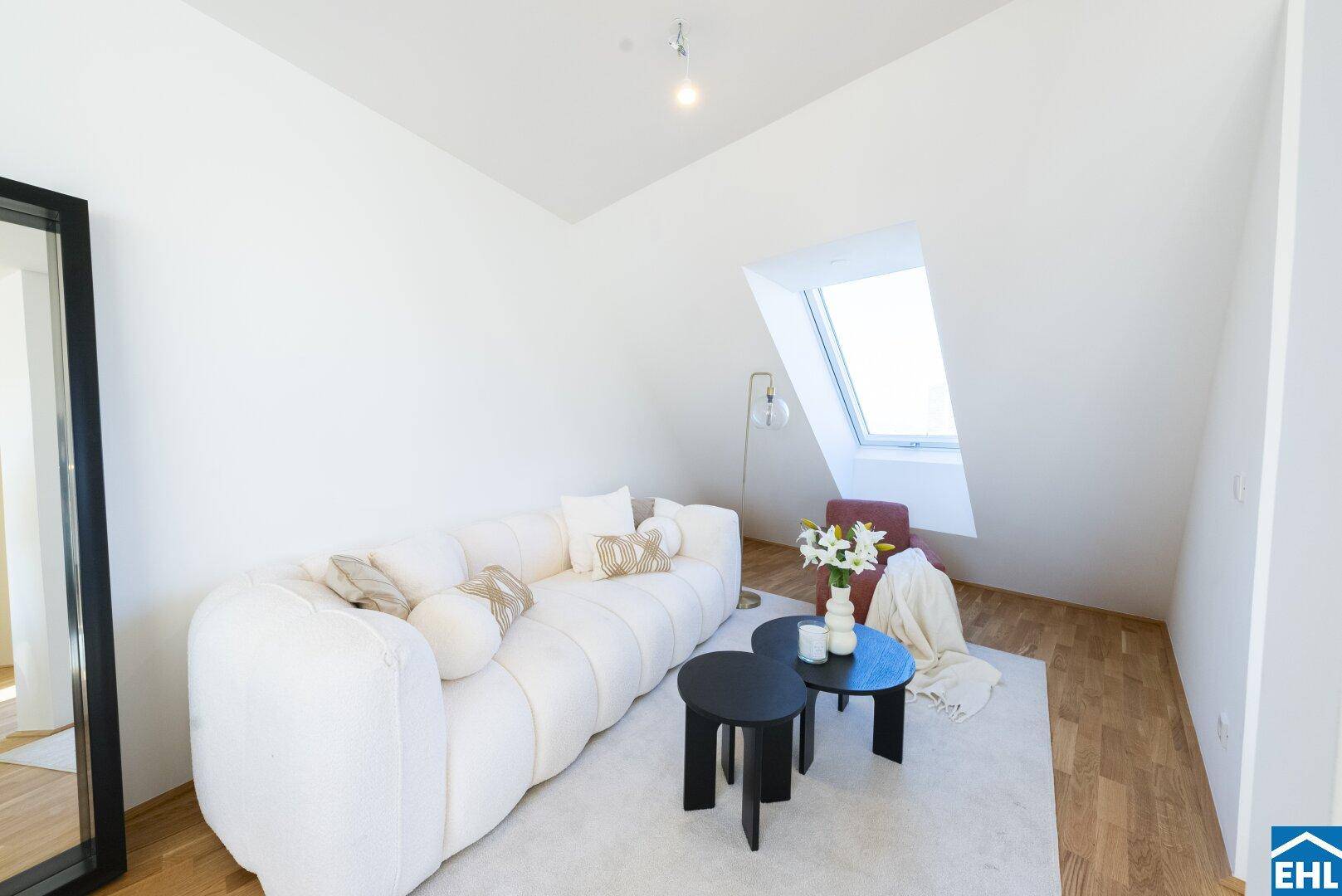Gemütliches Wohnzimmer im Dachgeschoss mit weißem Sofa, Holzboden und Dachfenster.