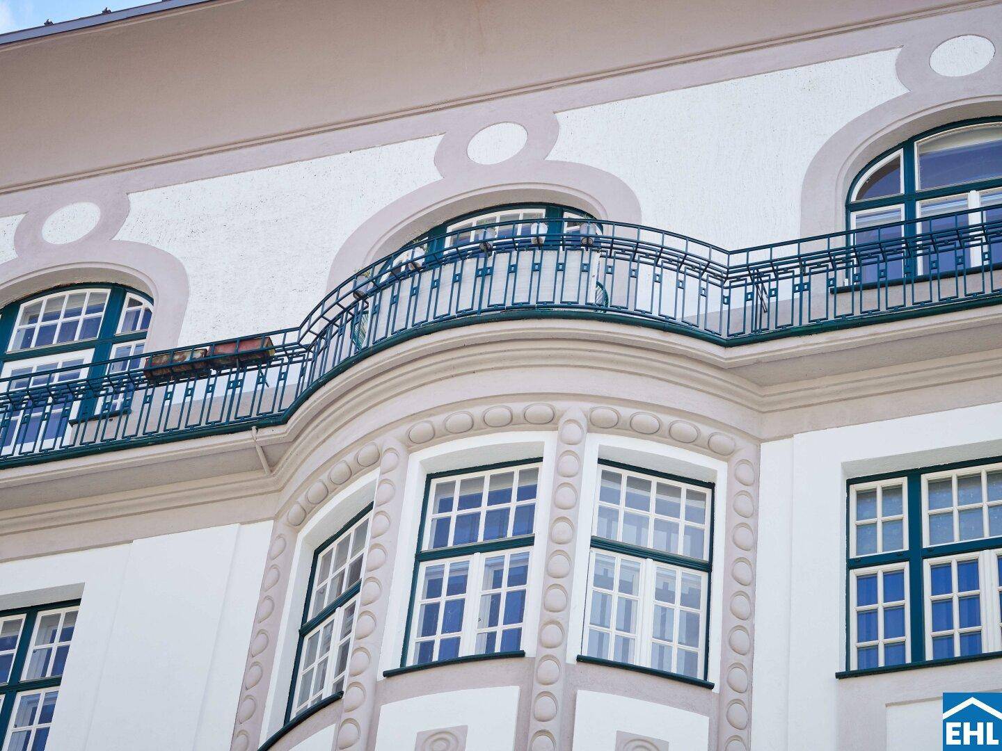 Detailansicht der historischen Fassade mit Stuckelementen, Bogenfenstern und schmiedeeisernem Balkongeländer.