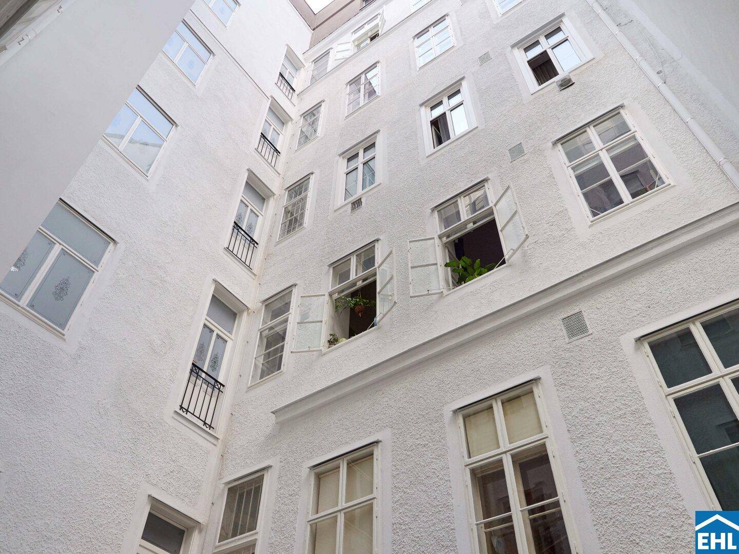 Blick nach oben in den hellen Innenhof mit zahlreichen Fenstern und weißer Fassade.