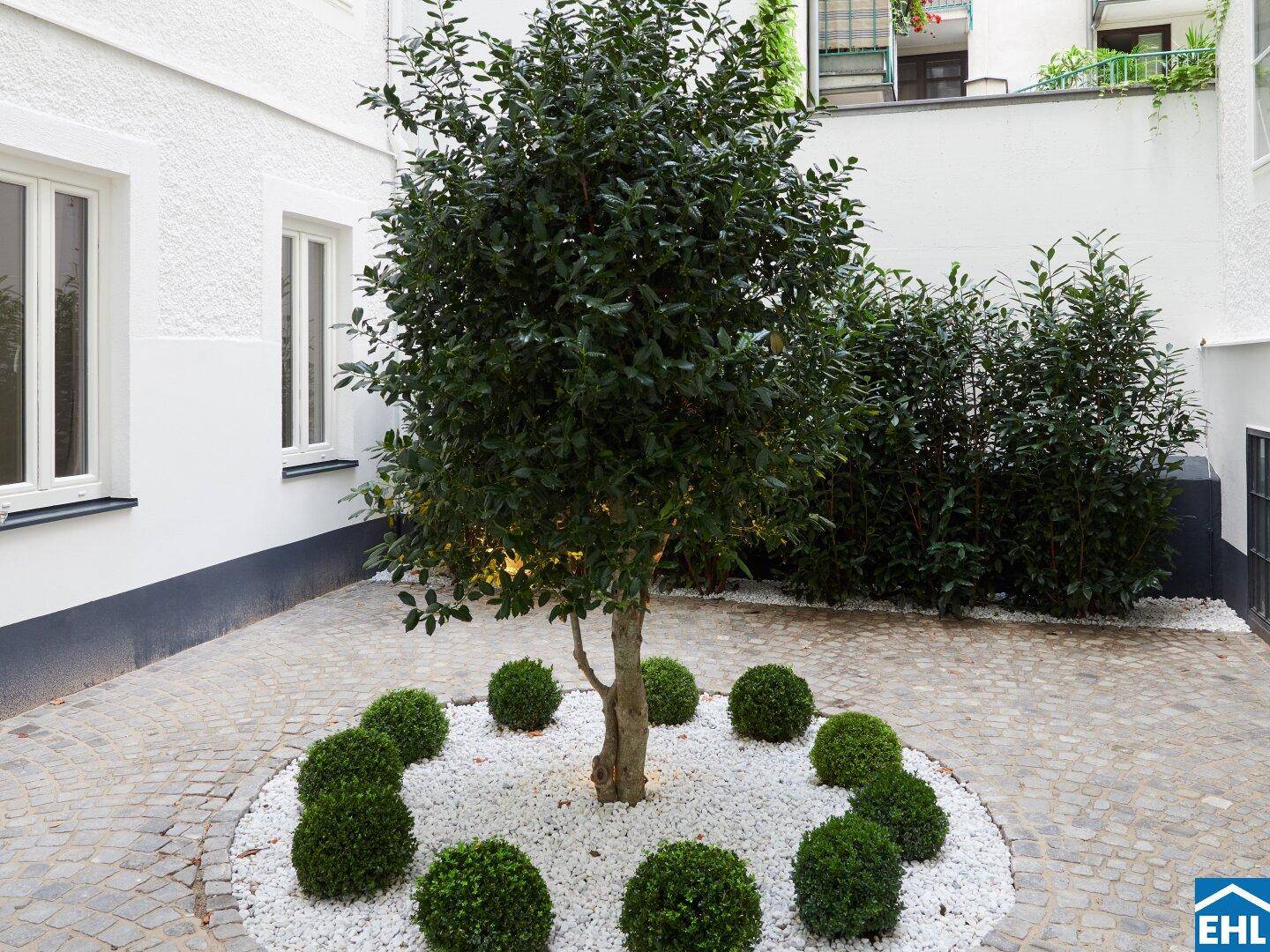 Gestalteter Innenhof mit Baum, Ziersträuchern und weißem Kiesbett.