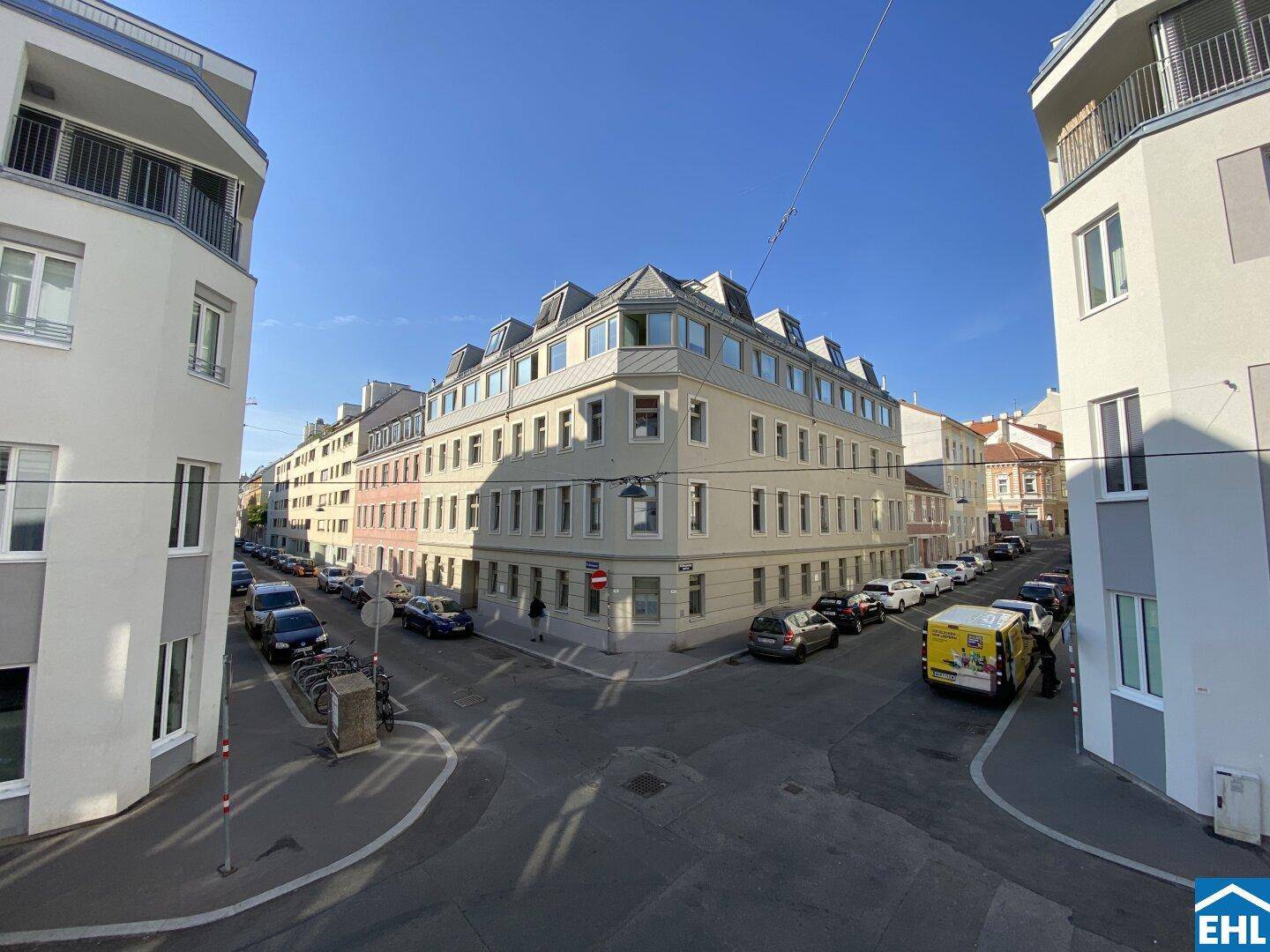 Blick auf die belebte Stadtstraße mit parkenden Autos und umliegenden Gebäuden.