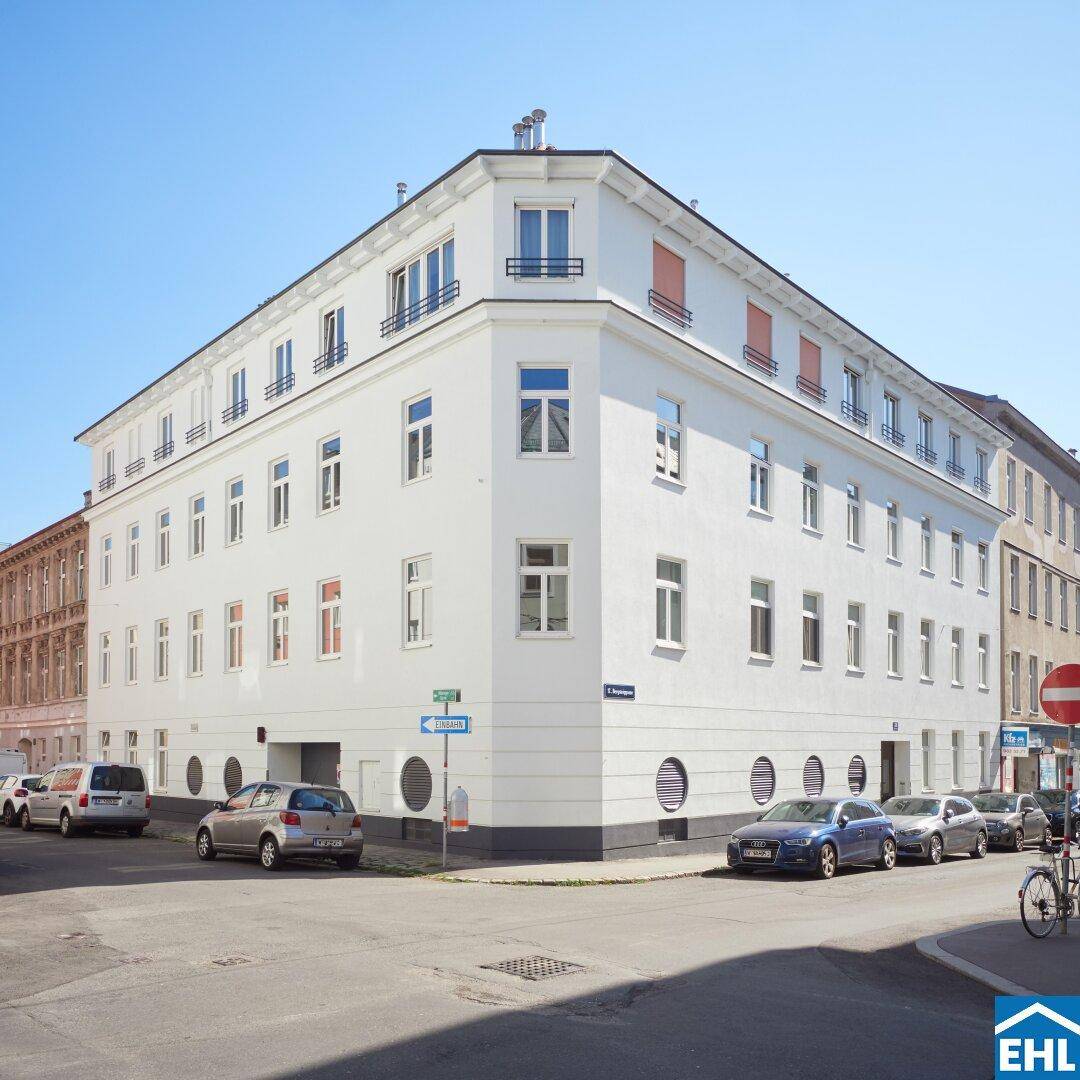 Modernes Eckgebäude mit weißer Fassade und vielen Fenstern an einer Stadtstraße.