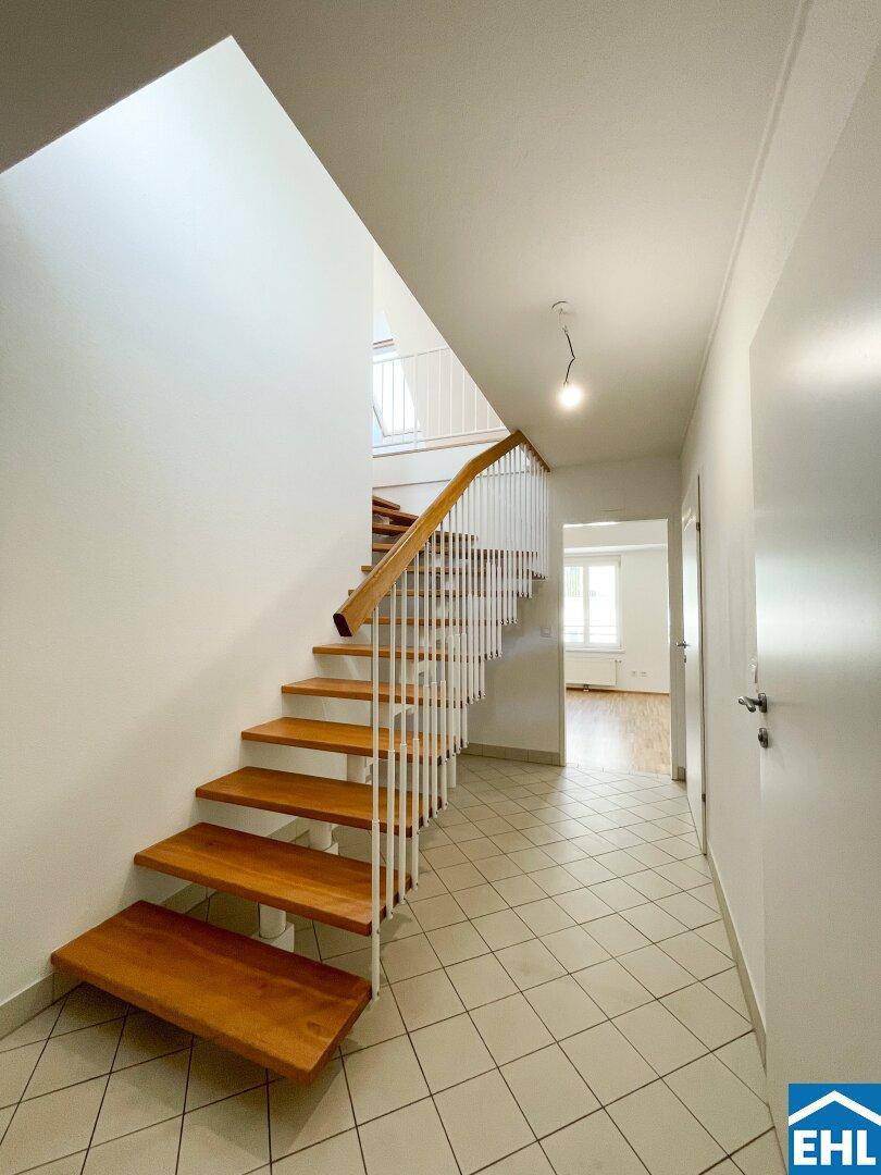 Heller Flur mit Holztreppe und Fliesenboden, der die verschiedenen Ebenen verbindet.