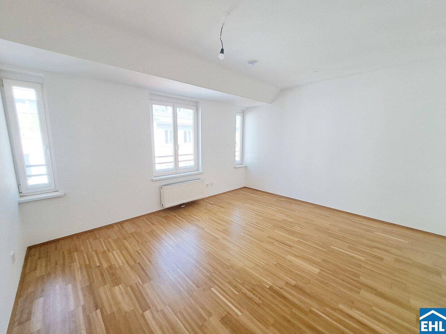 Geräumiges, helles Zimmer mit Parkettboden und großen Fenstern, ideal als Schlaf- oder Wohnzimmer.