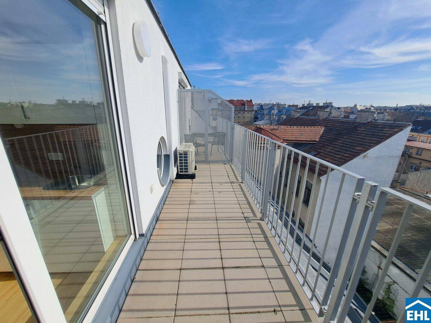 Sonniger Dachterrassenbereich mit Fliesenboden und Blick über die Dächer der Stadt.