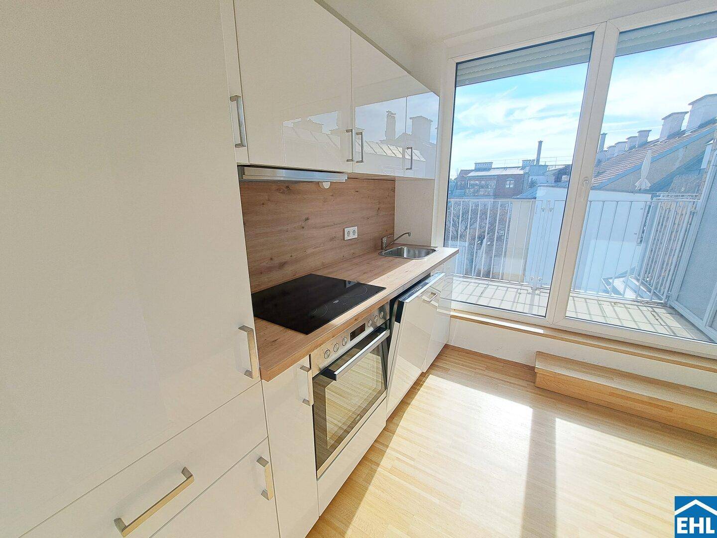 Moderne Einbauküche mit glänzenden weißen Fronten, Holzarbeitsplatte und Zugang zur Terrasse.