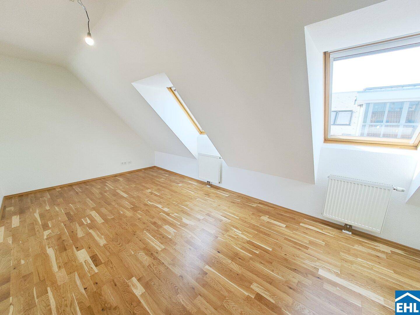 Dachgeschosszimmer mit schrägen Wänden, Parkettboden und Dachfenster für viel Licht.