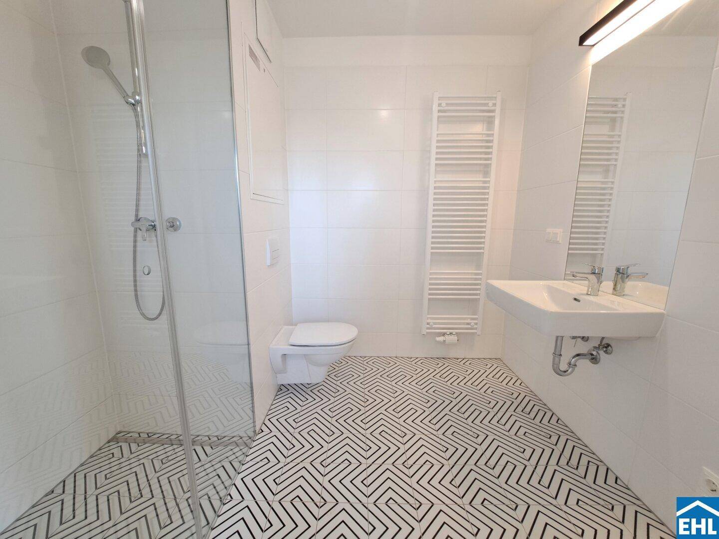 Modernes Badezimmer mit Duschkabine, Wand-WC, Waschbecken und Handtuchheizkörper.
