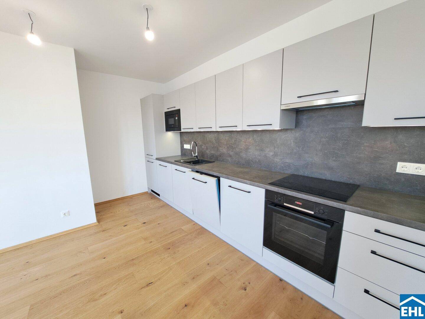 Moderne Einbauküche mit grauen Schränken, dunkler Arbeitsplatte und integrierten Geräten.