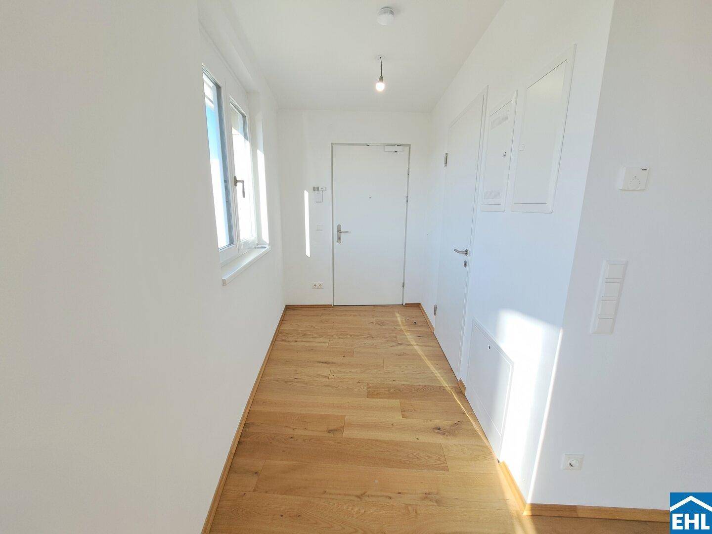 Heller Eingangsbereich mit Parkettboden, Fenster und weißer Eingangstür.