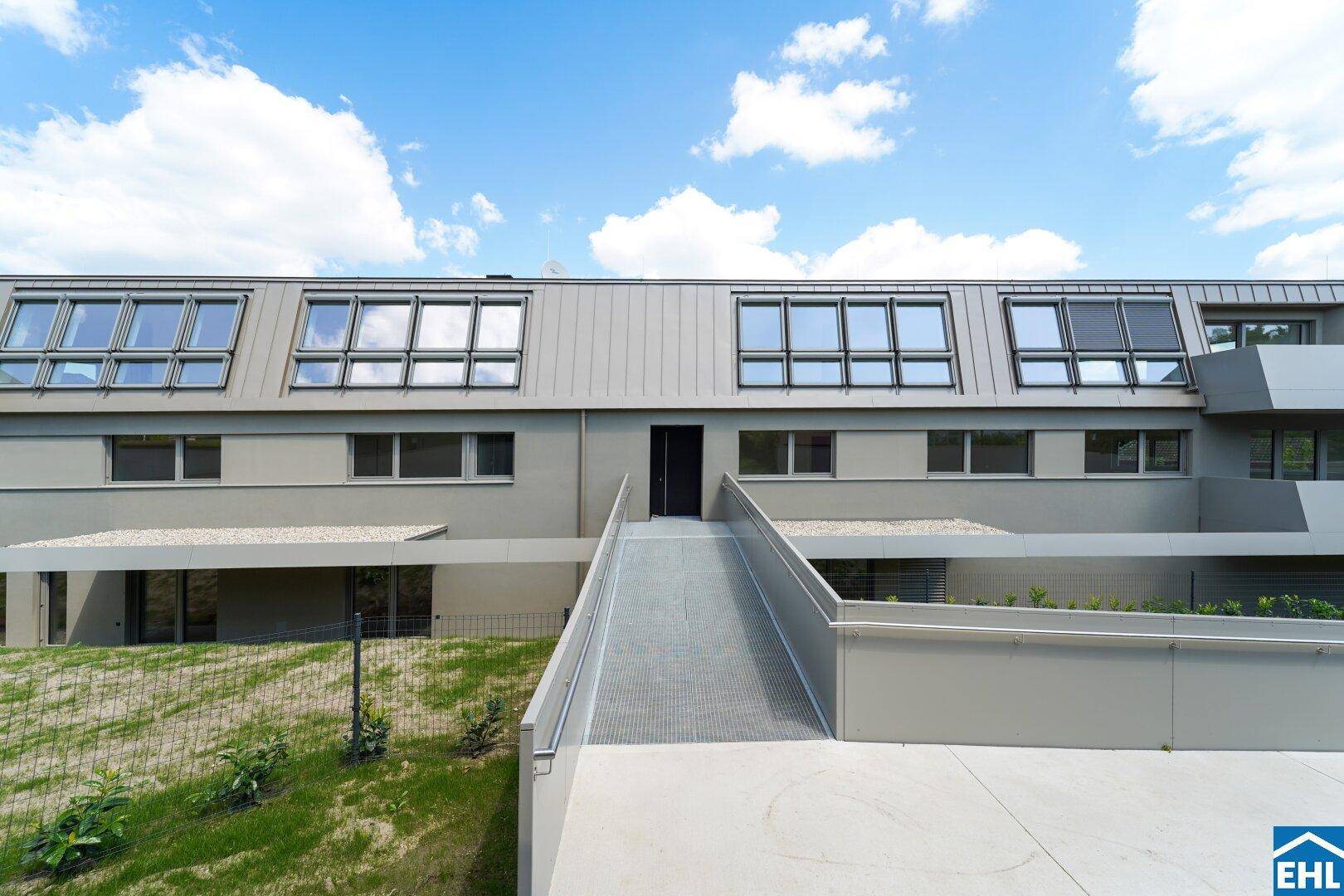 Moderne Gebäudefassade mit Rampe für barrierefreien Zugang und Dachfenstern.