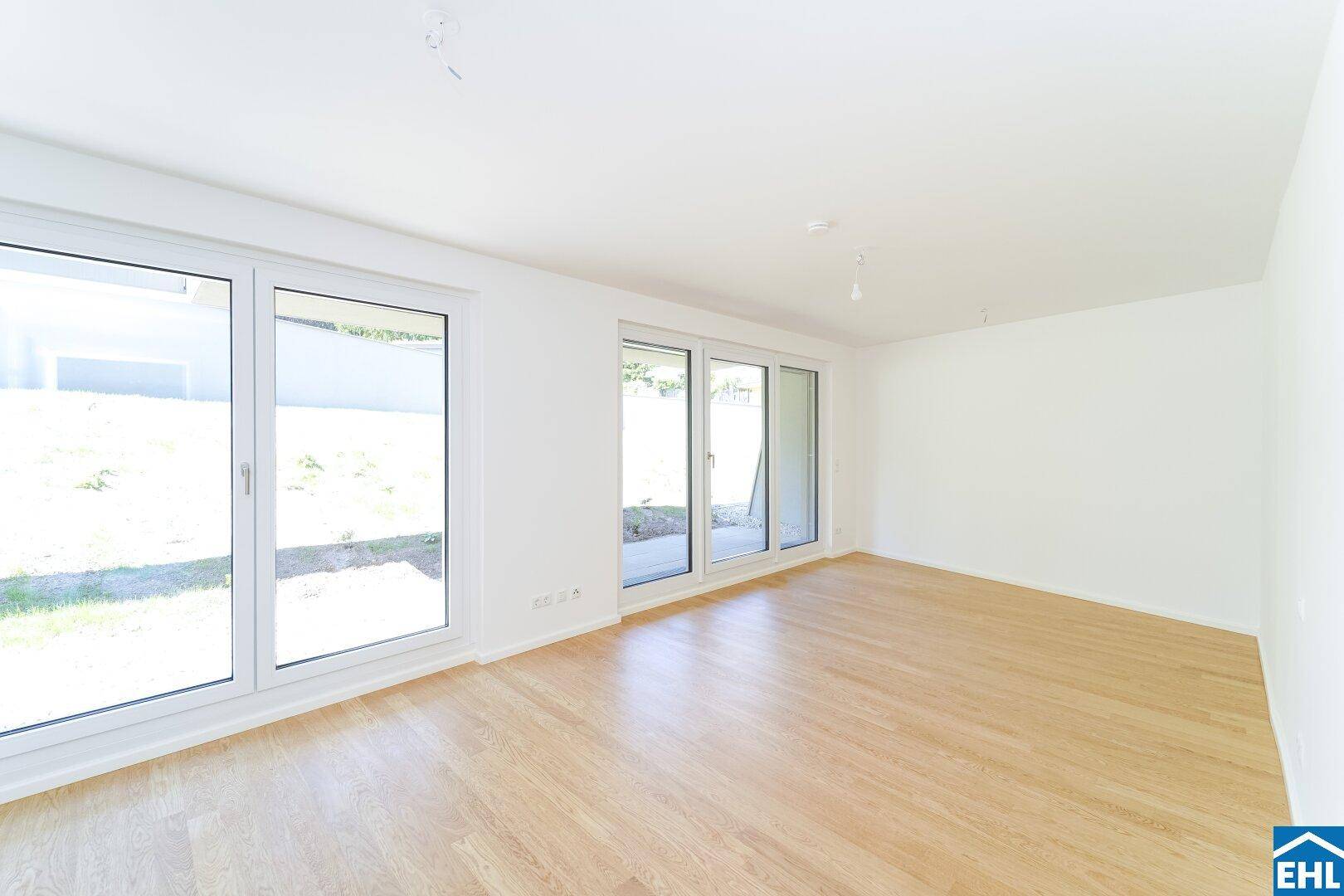 Heller Wohnraum mit Holzboden und großen Fenstern, die einen Blick auf die grüne Umgebung bieten.