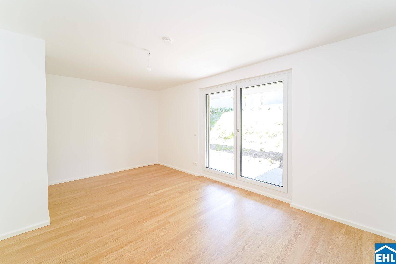 Helles Zimmer mit Holzboden und einem großen Fenster, das viel Tageslicht in den Raum lässt.