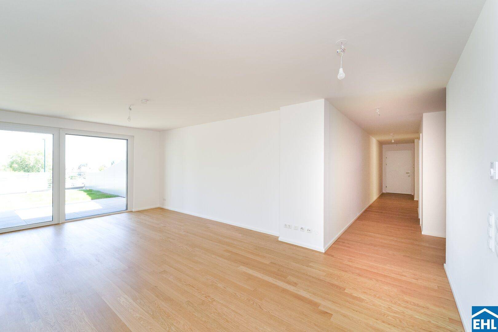Heller Wohnbereich mit Holzboden und Zugang zu einem langen Flur, der weitere Räume verbindet.