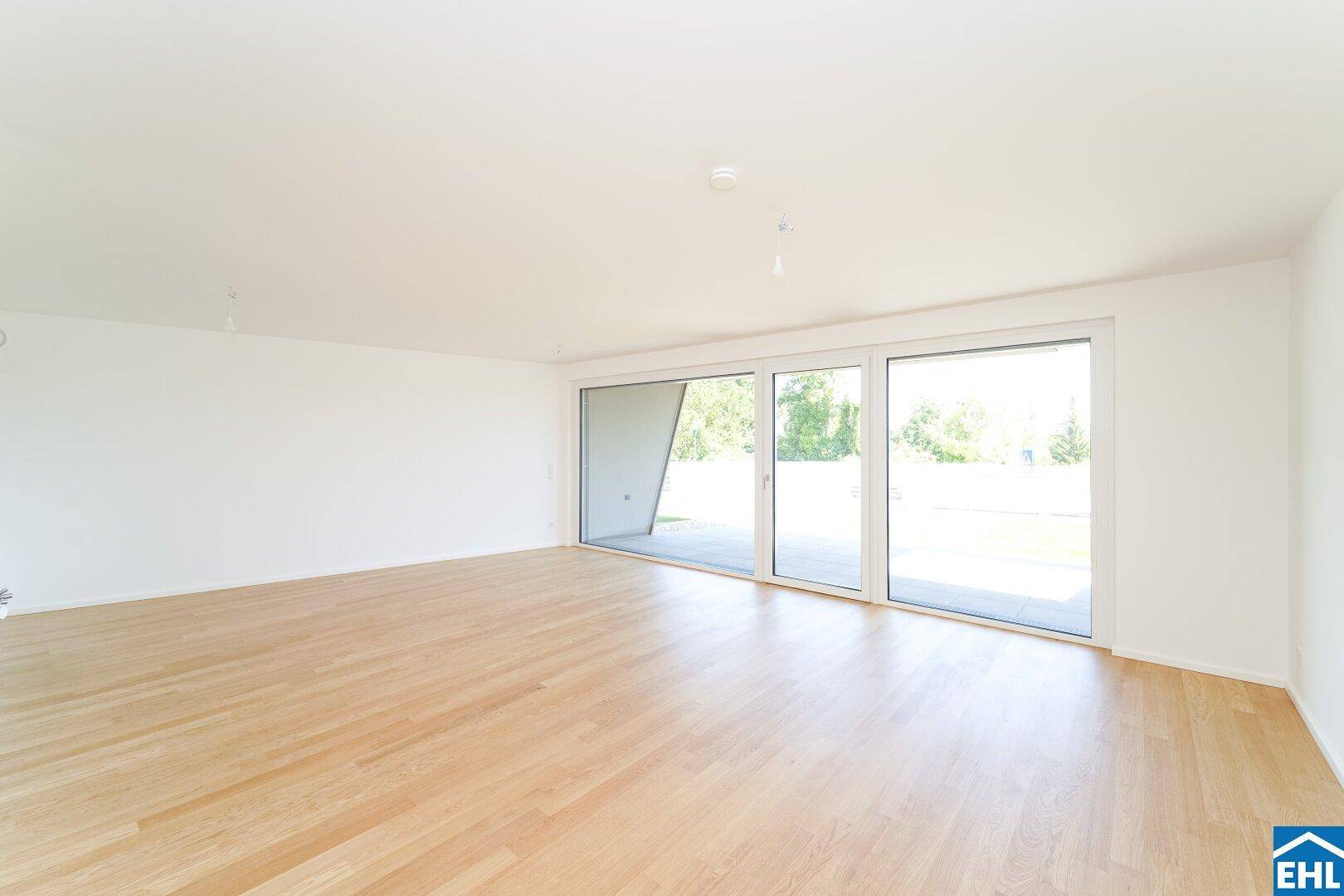Geräumiges Wohnzimmer mit Holzboden und breiten Fenstern, die viel Tageslicht hereinlassen.