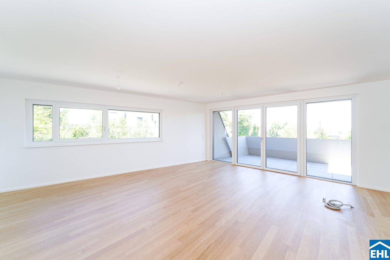 Helles Wohnzimmer mit Parkettboden, weißen Wänden und Zugang zu einem Balkon oder einer Terrasse.