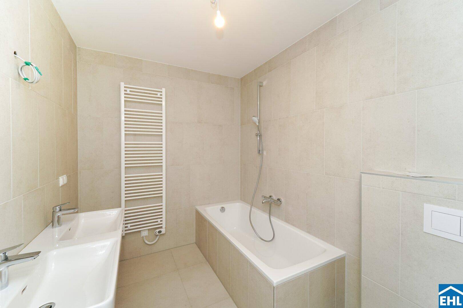 Modernes Badezimmer mit beigefarbenen Fliesen, Badewanne, Doppelwaschbecken und Handtuchheizkörper.