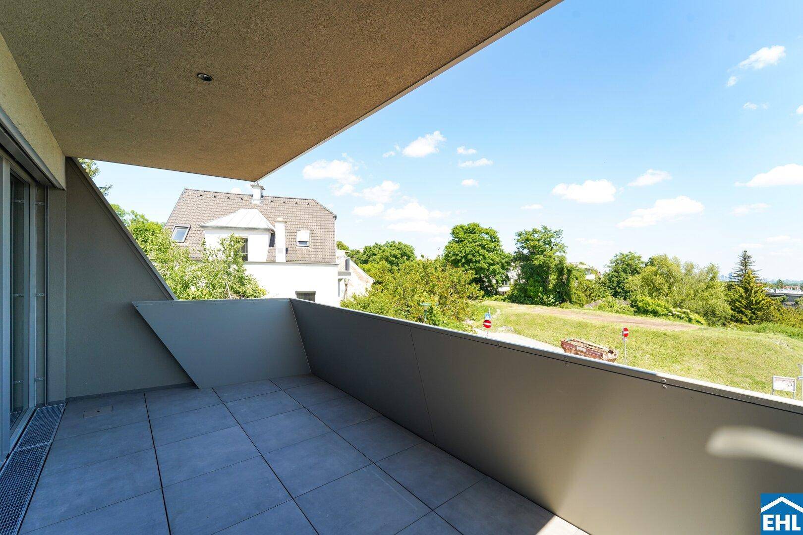 Moderner Balkon mit grauen Fliesen und einem weiten Blick ins Grüne und auf die Umgebung.