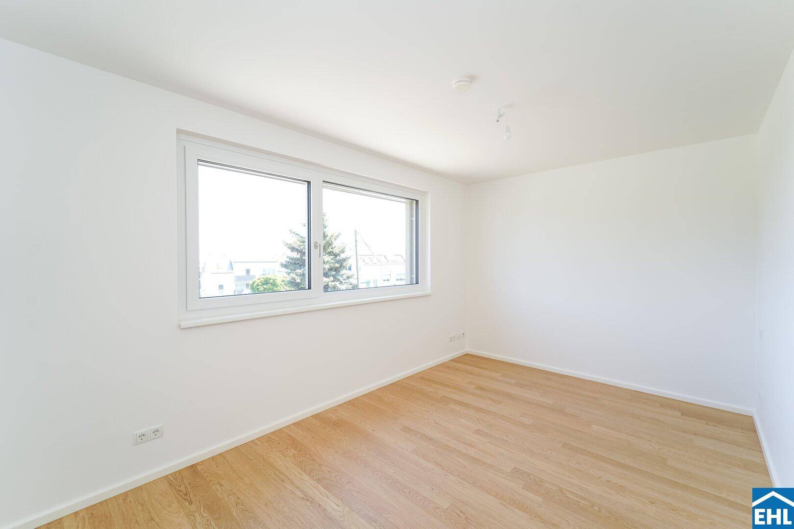 Geräumiges, unmöbliertes Zimmer mit hellem Holzboden und großen Fenstern für viel Tageslicht.