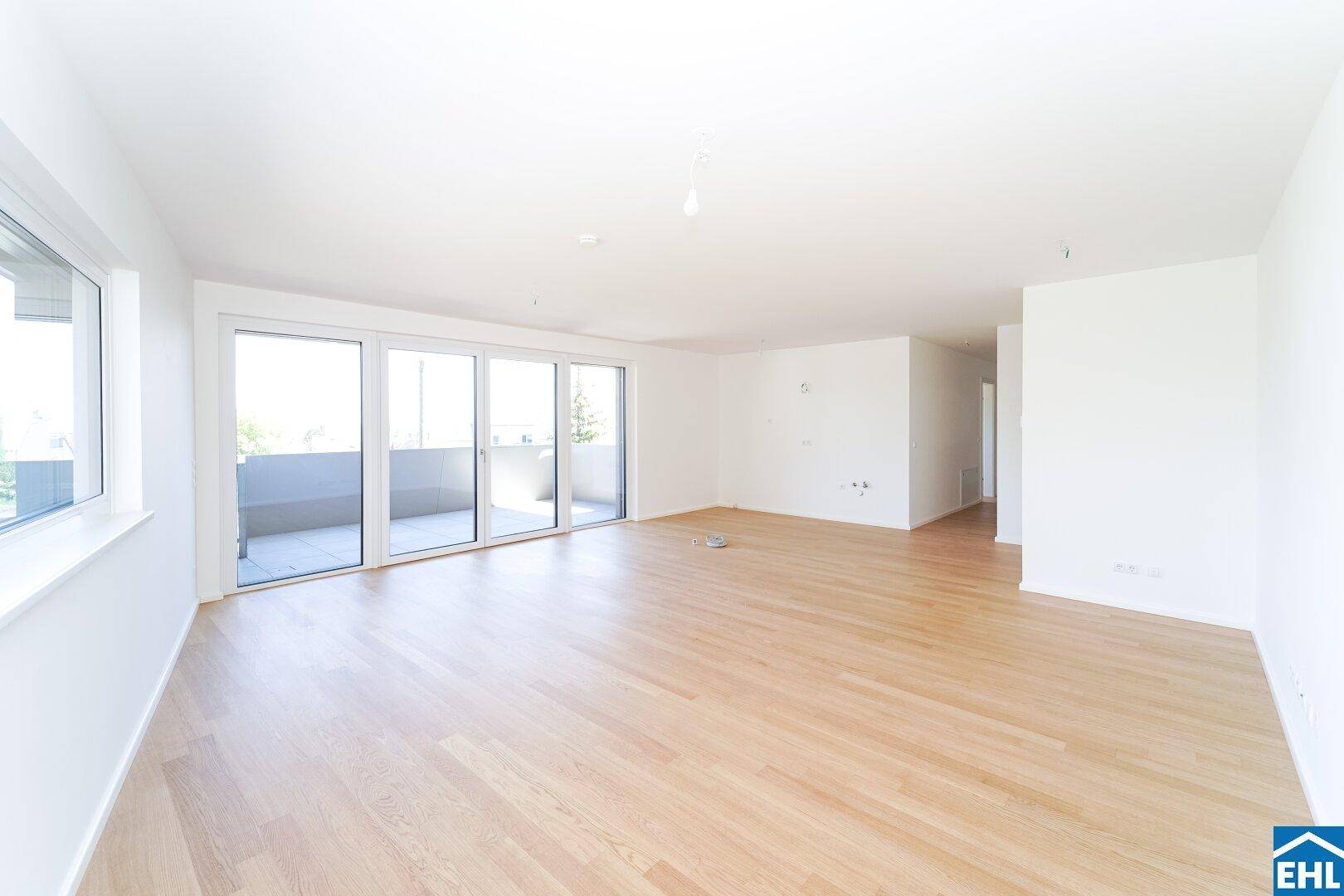 Geräumiges, helles Wohnzimmer mit Holzboden und großen Fenstern, die viel Tageslicht hereinlassen.