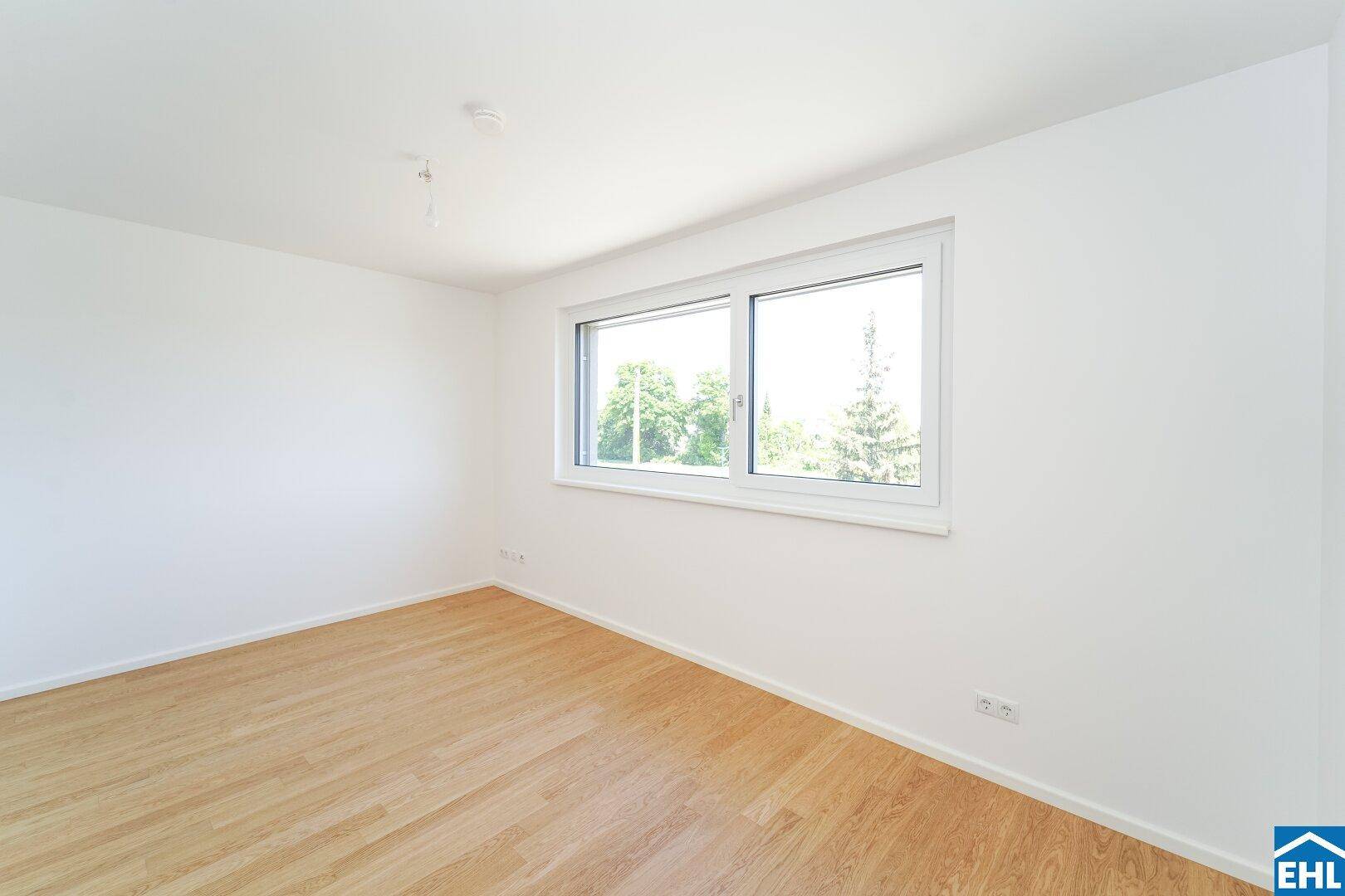 Helles Schlafzimmer mit Parkettboden und Blick ins Grüne durch das Fenster.