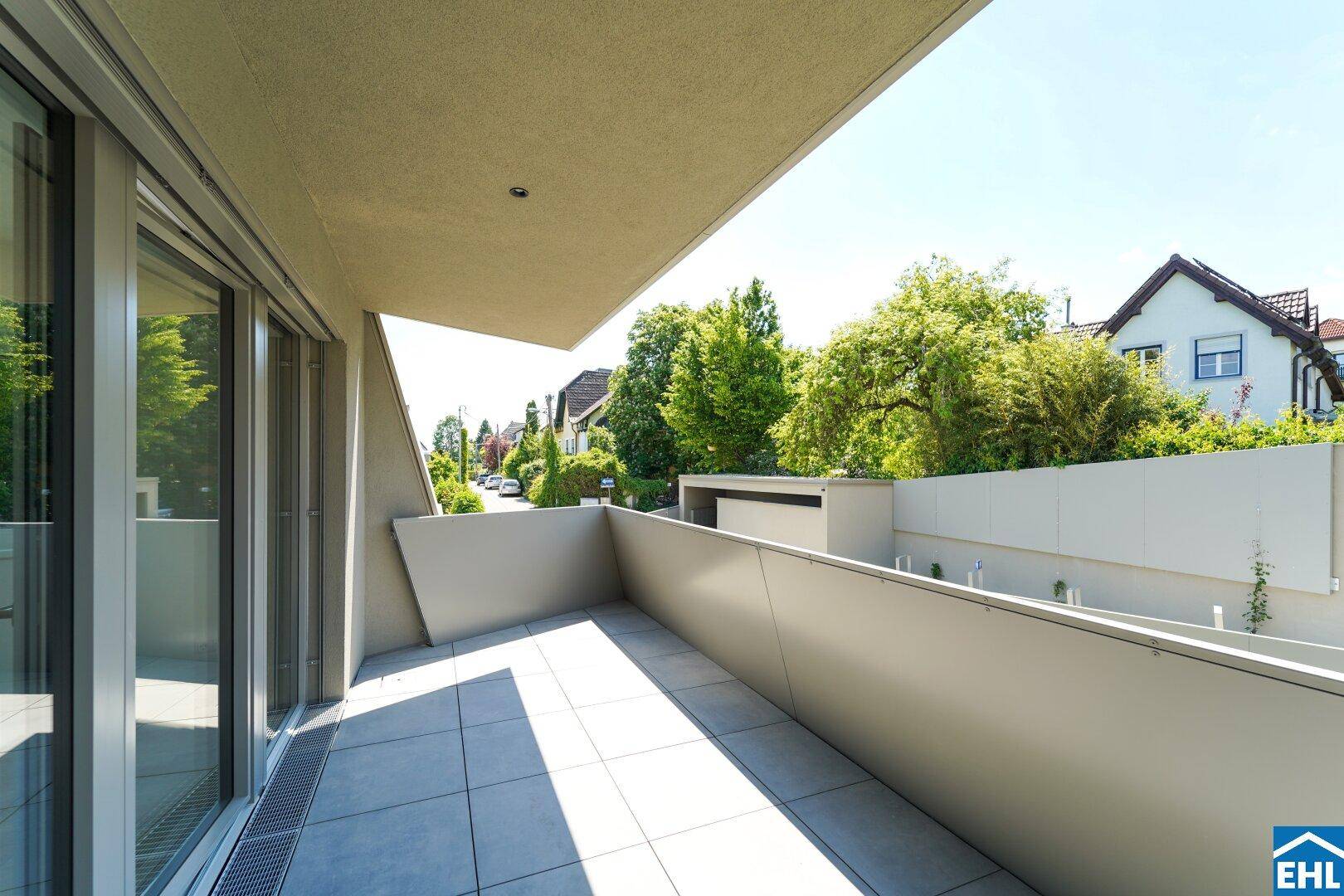 Sonniger Balkon mit Fliesenboden und Blick auf die grüne Umgebung.