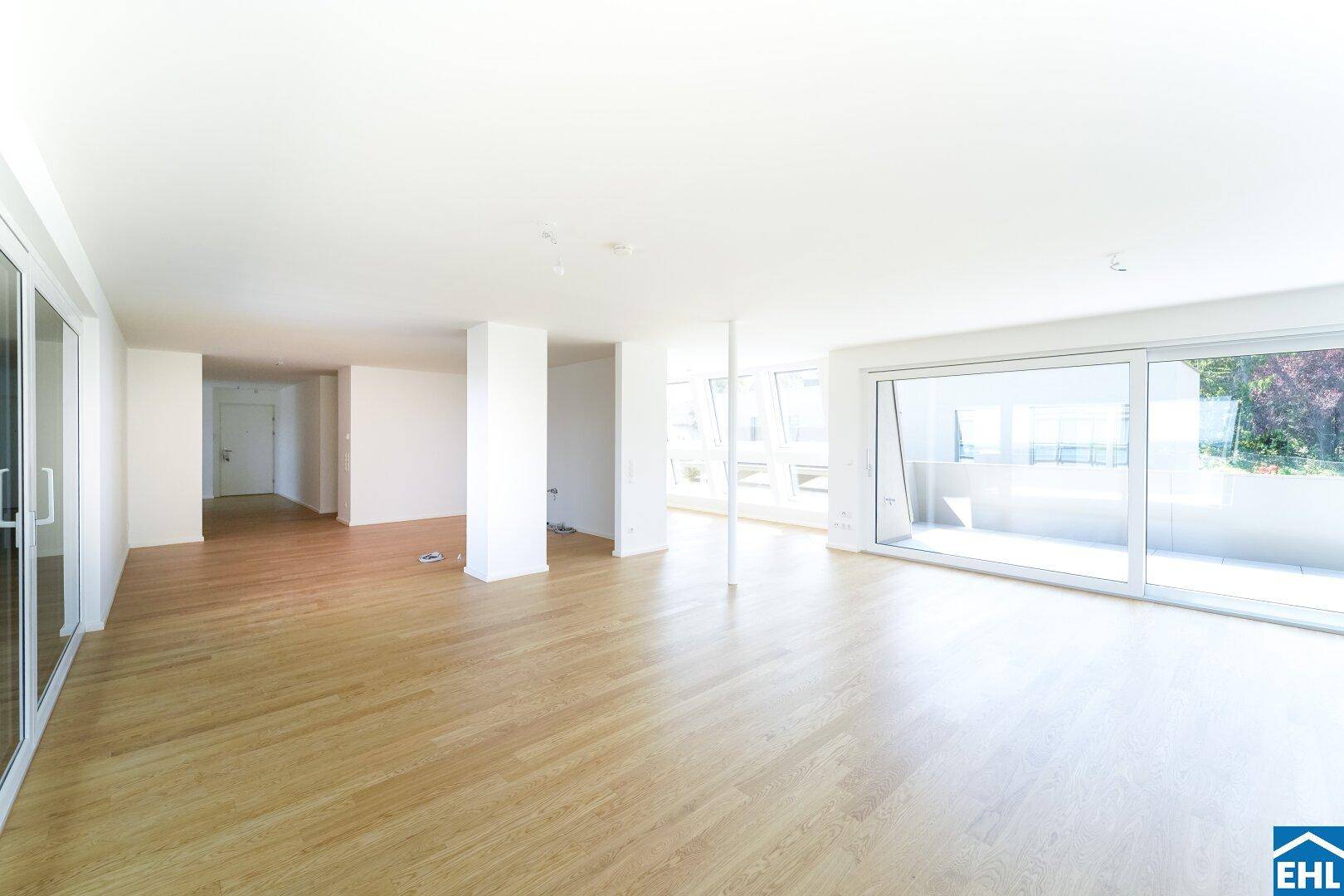Weitläufiger Wohnraum mit großen Fensterfronten und hellem Holzfußboden, ideal für offenes Wohnen.