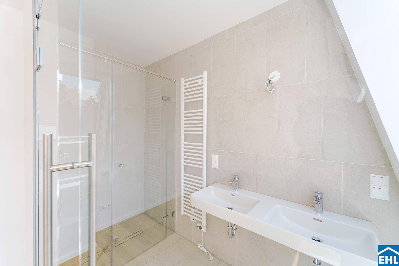 Elegantes Badezimmer mit Doppelwaschbecken, beheiztem Handtuchhalter und geräumiger Glasdusche.