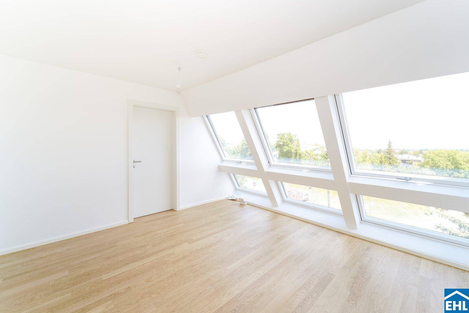 Schlafzimmer im Dachgeschoss mit schrägen Fenstern, die viel Tageslicht hereinlassen und Holzboden.