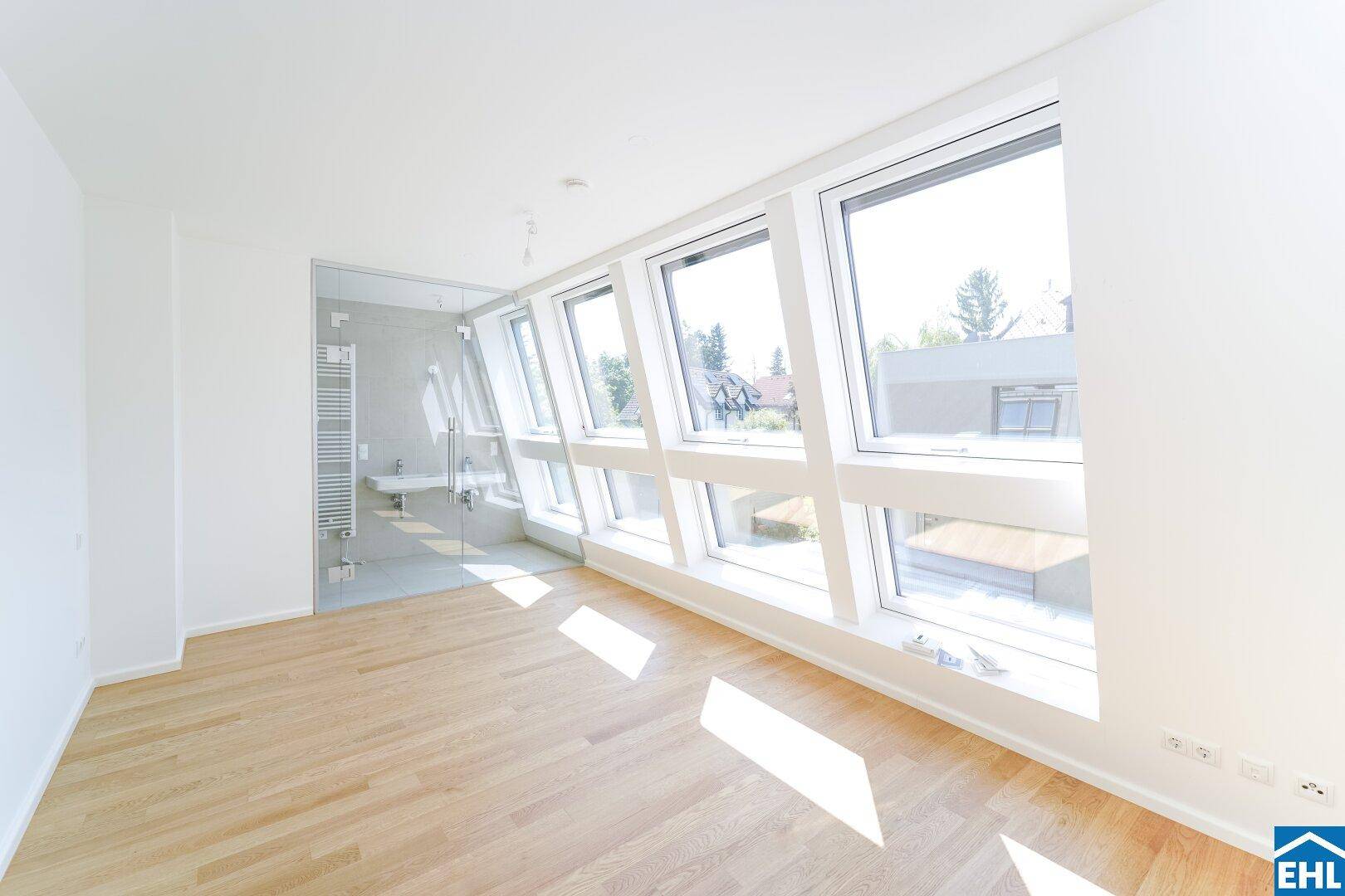 Helles Schlafzimmer mit schrägen Fenstern und Holzboden, angrenzend an ein modernes Badezimmer.