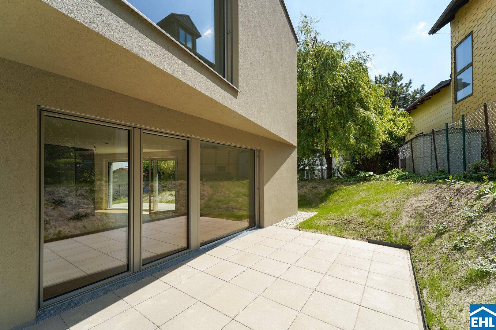 Helle Terrasse mit Fliesenboden und direktem Zugang zum grünen Gartenbereich.
