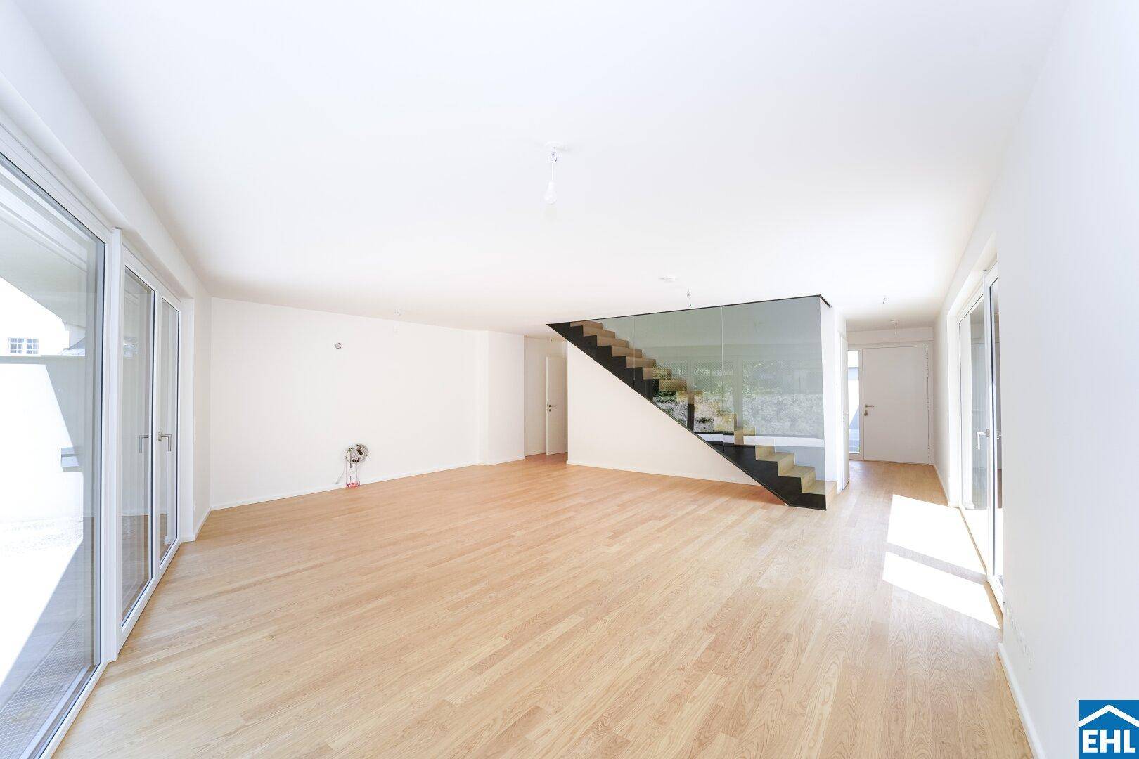 Geräumiger Wohnbereich mit moderner Treppe, hellen Wänden und viel Tageslicht.