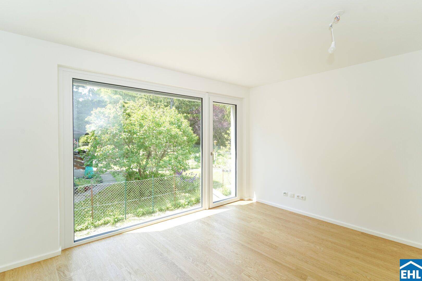 Heller Raum mit Parkettboden und großem Fenster mit Blick ins Grüne.