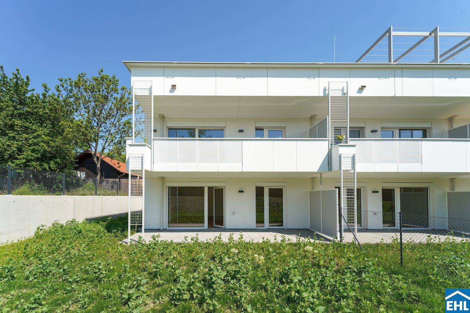 Moderne Wohnanlage mit hellen Fassaden, Balkonen und Terrassen, umgeben von einer grünen Umgebung.