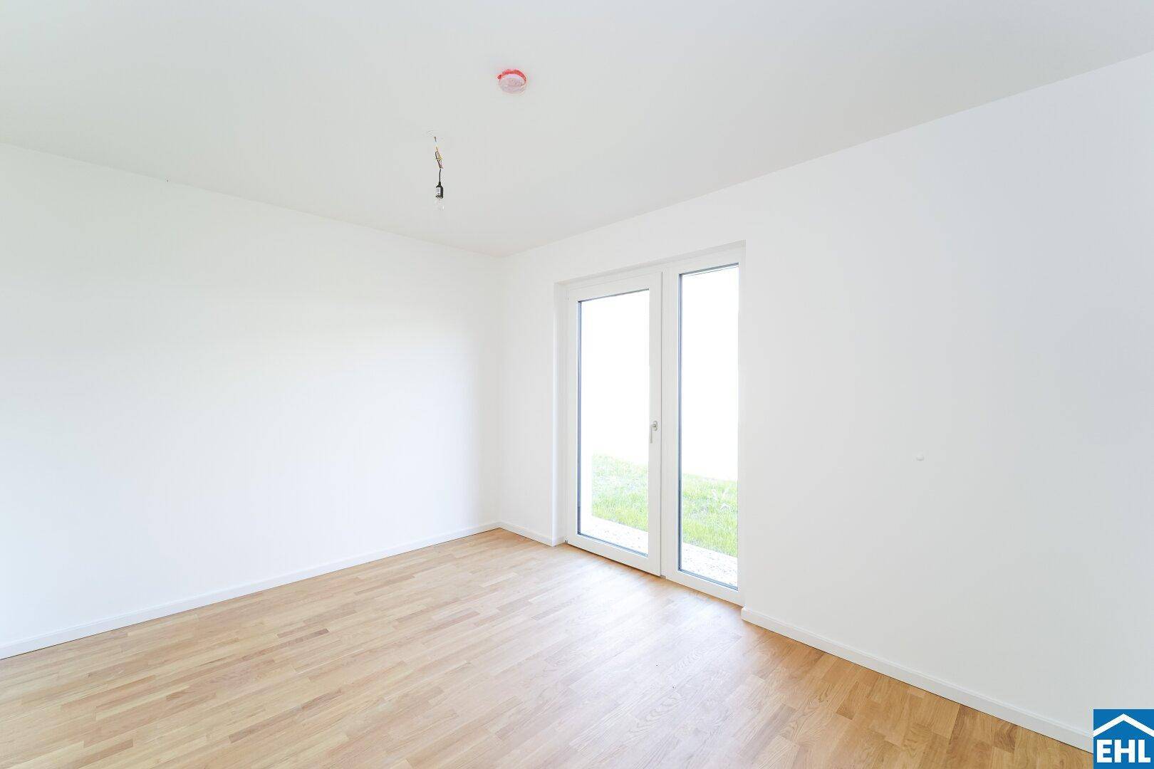 Helles Zimmer mit Parkettboden und großem Fenster, das viel Tageslicht hereinlässt.