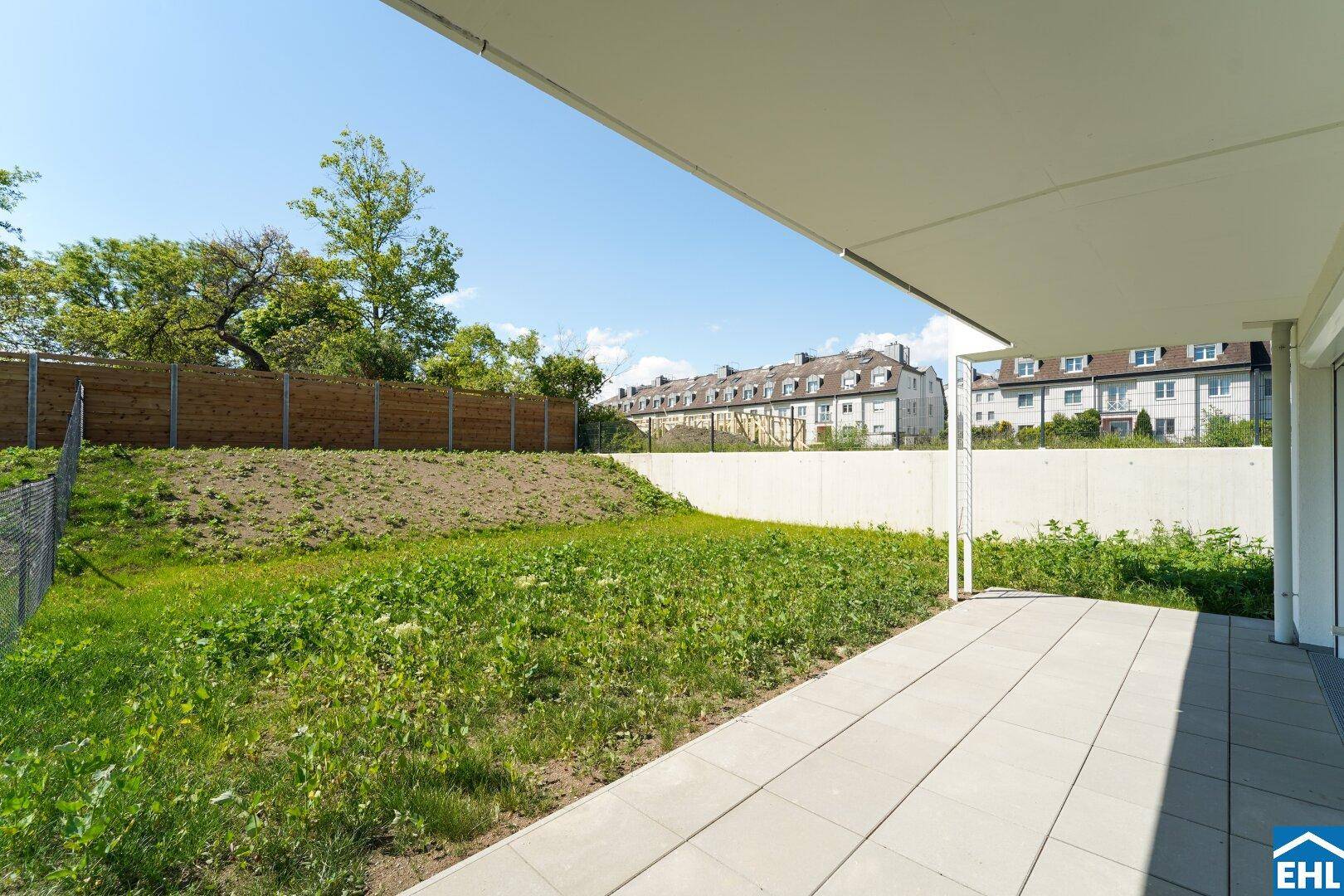 Geräumige Terrasse mit grauen Fliesen und angrenzender Rasenfläche, ideal für Entspannung im Freien.