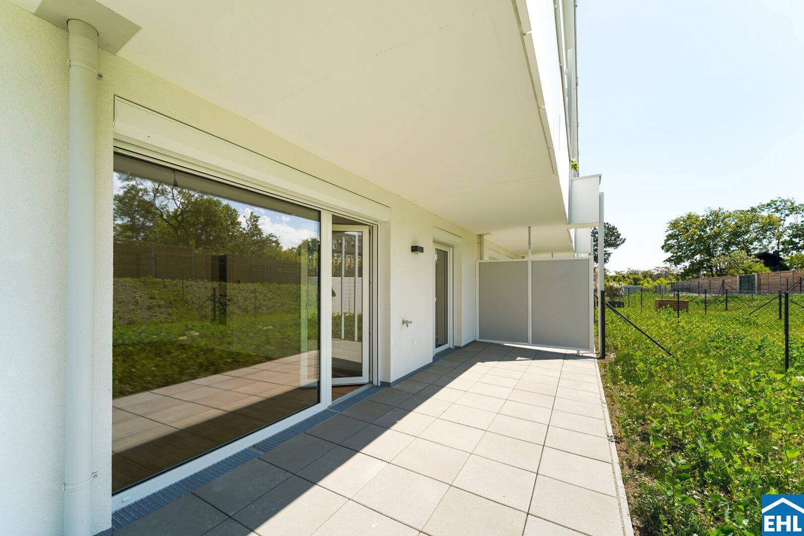 Breite Terrasse mit Zugang vom Wohnbereich und Blick auf die umliegende Grünfläche.