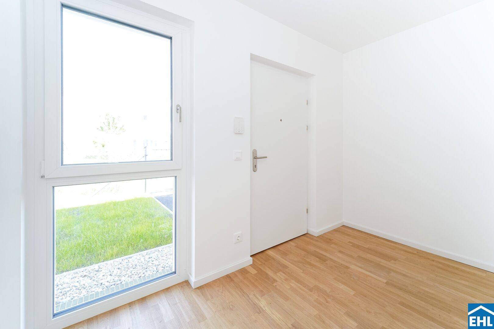 Eingangsbereich oder Flur mit hellem Parkettboden, weißer Tür und Fenster mit Blick ins Grüne.