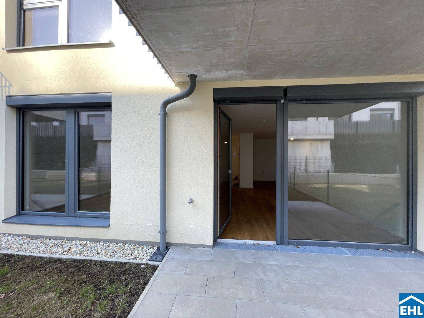 Moderne Terrasse mit großen Fenstertüren und Rollläden, die direkten Zugang zum Innenbereich bietet.