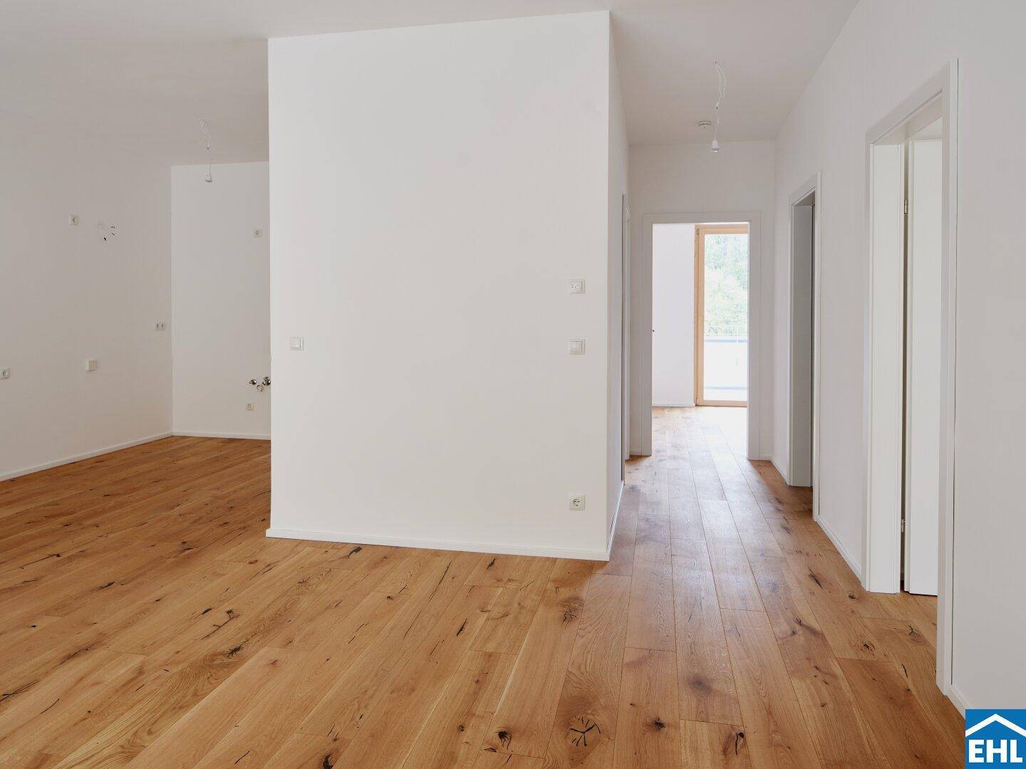 Heller Flur mit Holzboden und weißen Wänden, der zu verschiedenen Räumen im Neubau führt.