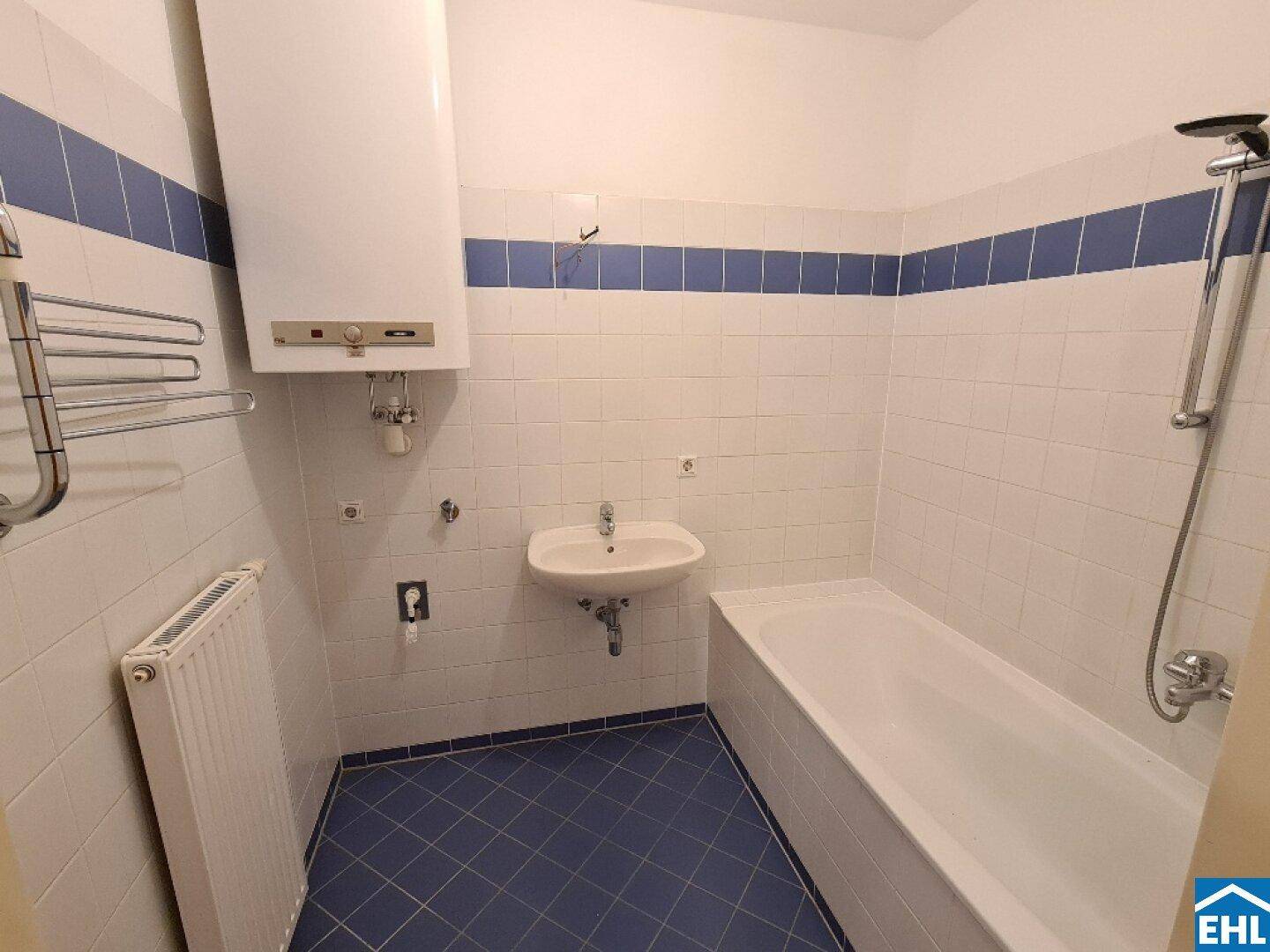 Badezimmer mit Badewanne, Waschbecken und Wandfliesen in Weiß und Blau, ausgestattet mit Warmwasserboiler.