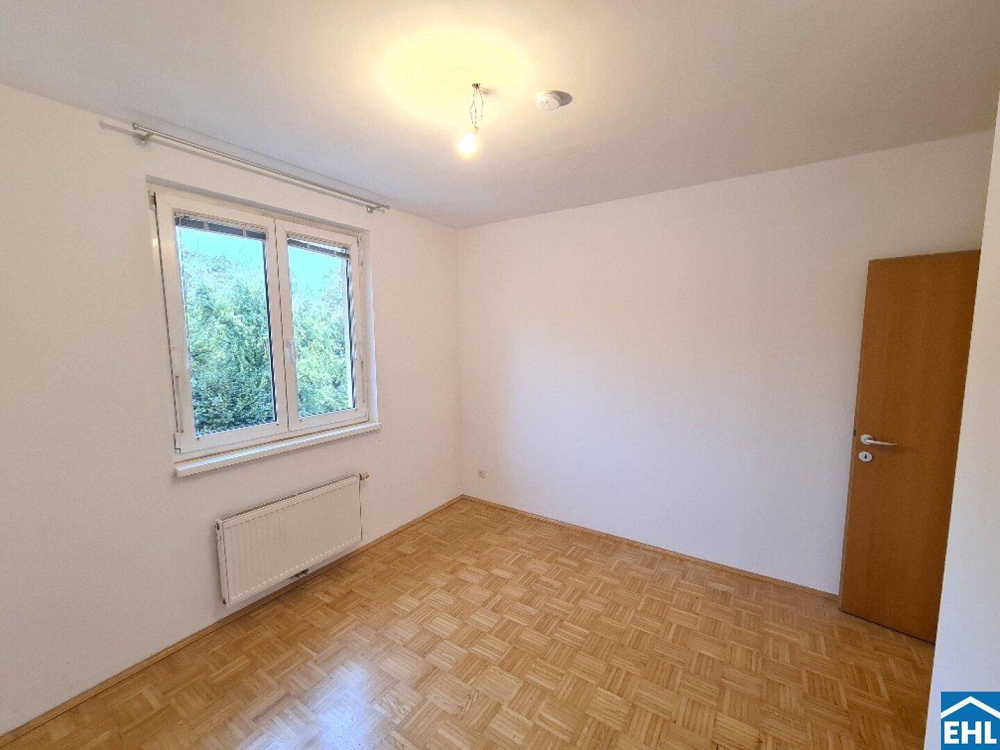 Freundliches Zimmer mit Parkettboden und großem Fenster, bietet viel Tageslicht und eine angenehme Atmosphäre.
