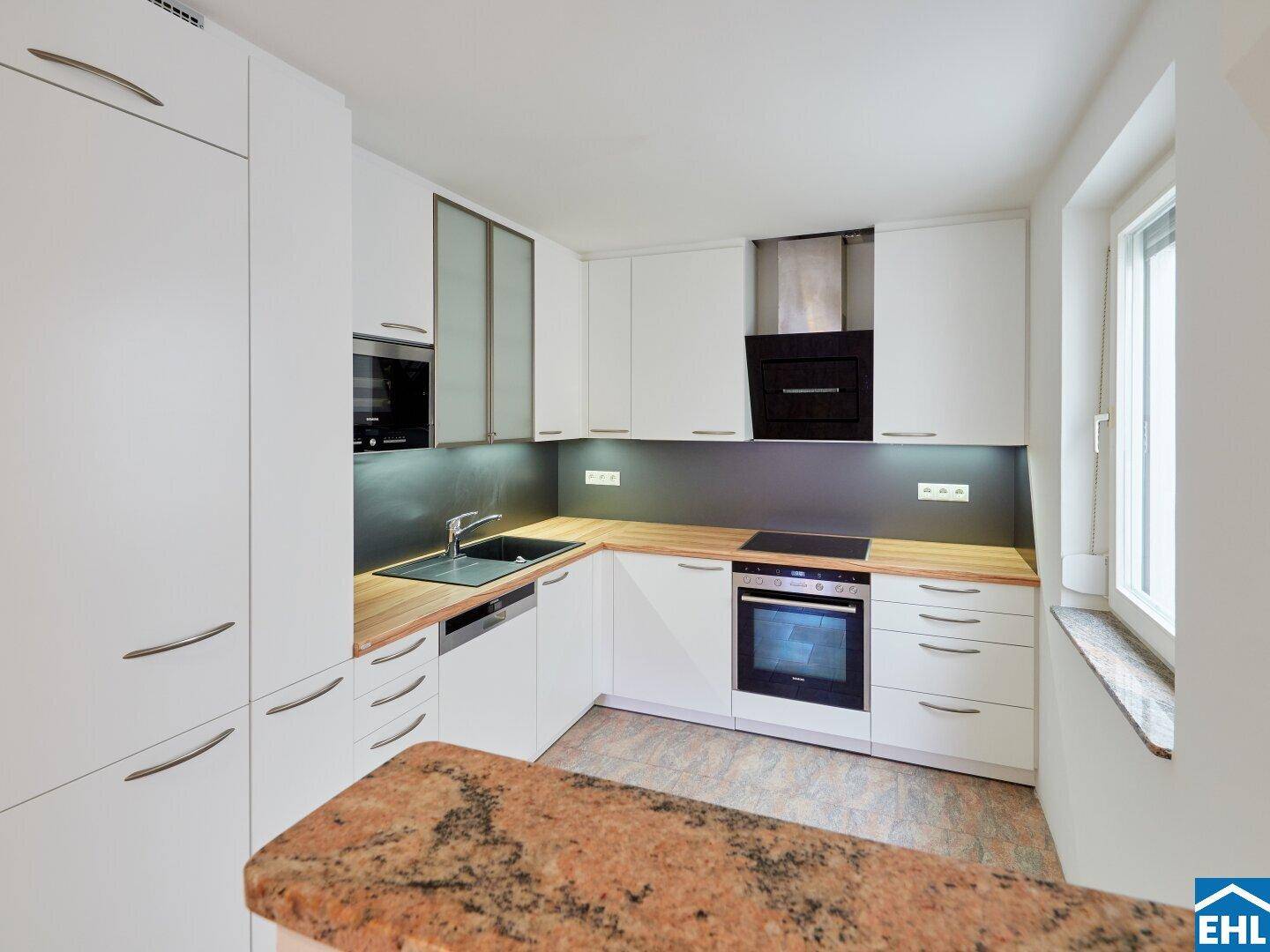 Moderne Einbauküche mit weißen Schränken, Holztheke und Granitarbeitsplatte, ausgestattet mit Premium-Geräten.