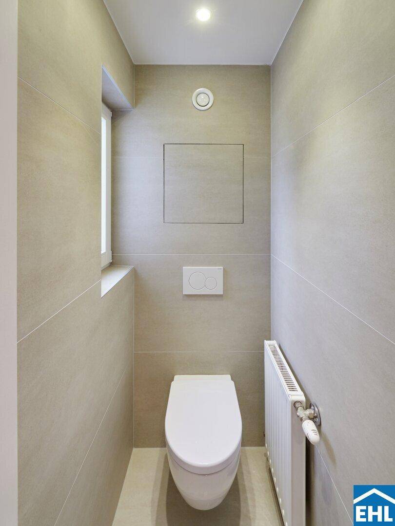 Modernes Gäste-WC mit Wand-WC, Fenster und hellen Fliesen, sehr sauber und funktional gestaltet.
