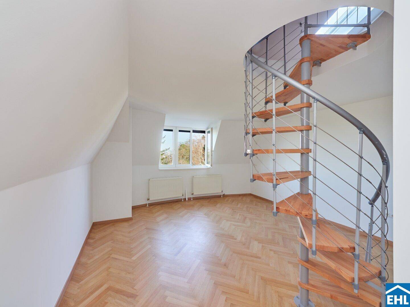 Geräumiger Dachgeschossraum mit eleganter Wendeltreppe und Blick ins Grüne durch das Fenster.