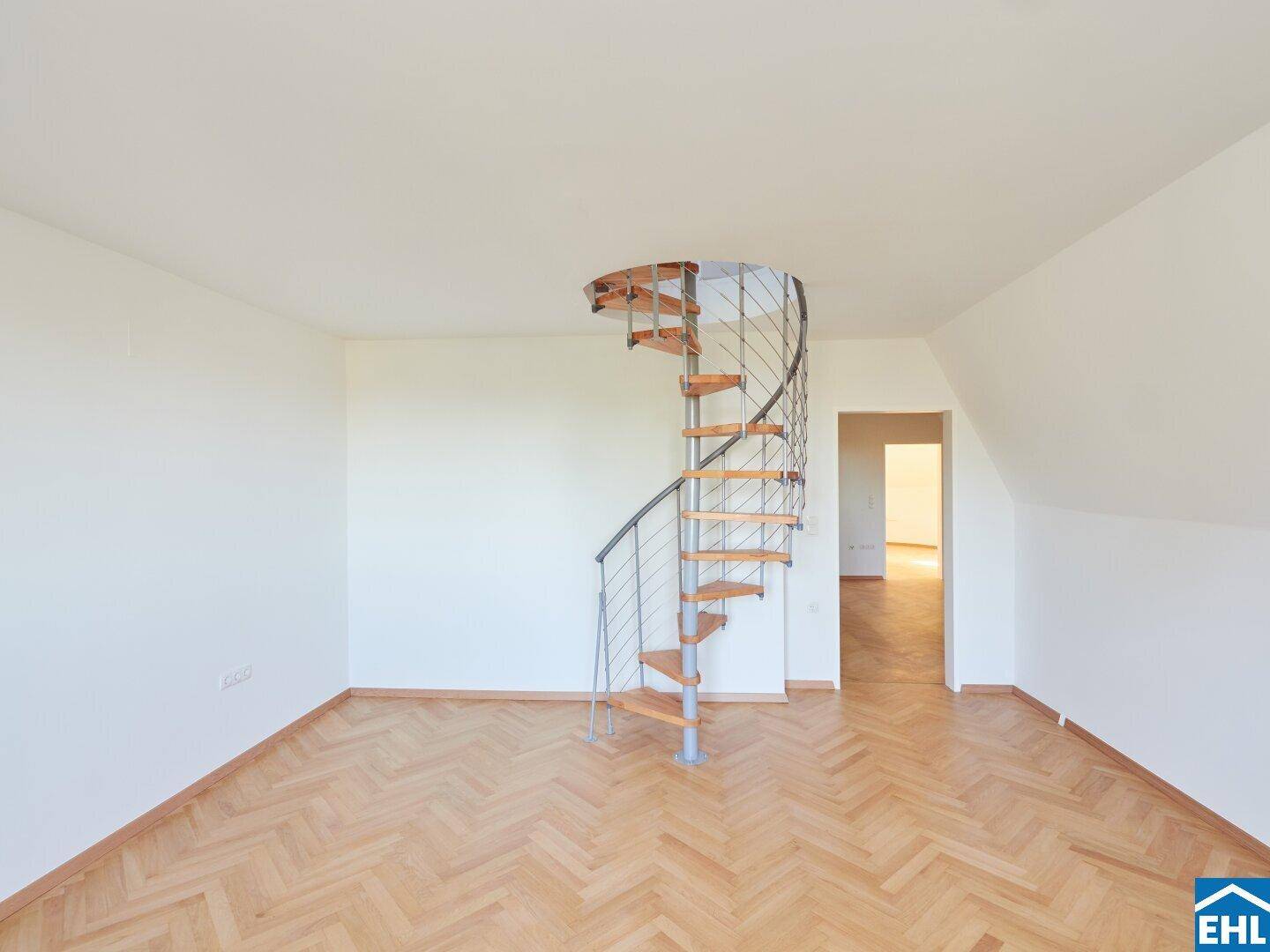 Offener Dachgeschossraum mit moderner Wendeltreppe und klassischem Fischgrätparkettboden.