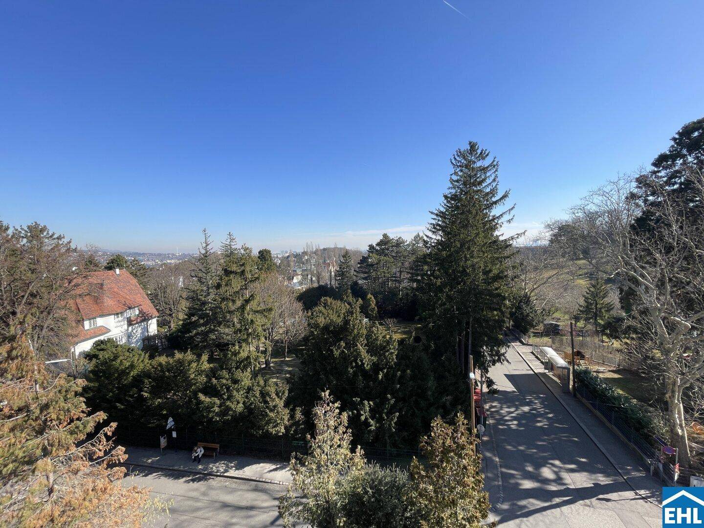 Weitläufiger Blick über grüne Baumwipfel und die Stadt am Horizont unter einem klaren blauen Himmel.