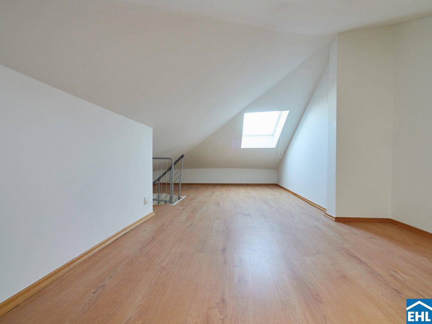 Langer Dachgeschossraum mit Laminatboden, schrägen Wänden und einem Dachfenster für natürliche Belichtung.