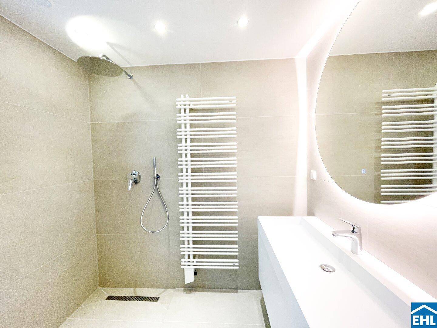 Modernes Badezimmer mit begehbarer Regendusche, beheiztem Handtuchhalter und großem, beleuchtetem Spiegel.