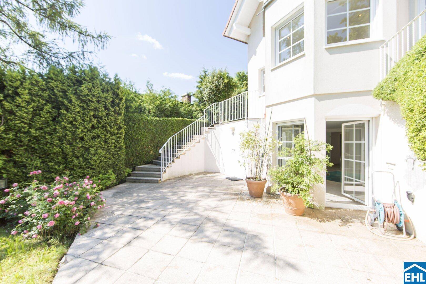 Große gepflasterte Terrasse am Haus mit Zugang zum Garten und geschwungenem Treppenaufgang.